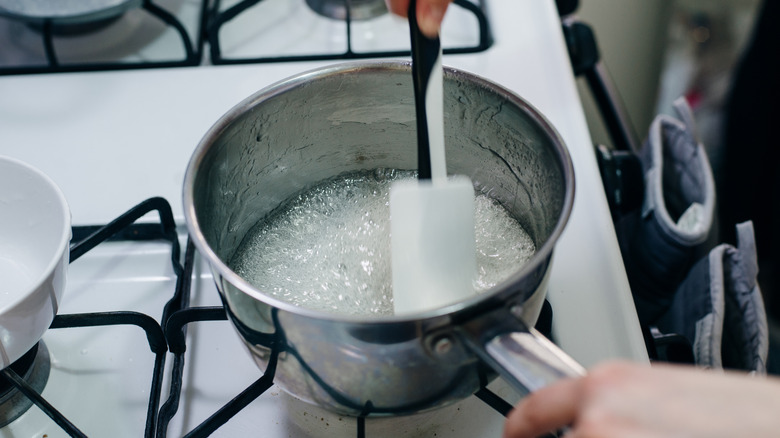 A chef stirs a white spatula in a stainless steel saucepan full of wet caramel