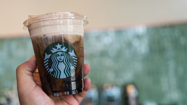 Someone holds up an iced coffee with cold foam
