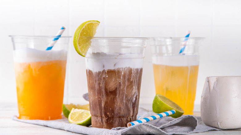 Three dirty sodas sitting in a row, two orange and one with traditional cola.