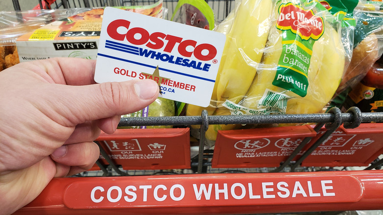 Hand holding Costco card with Costco grocery cart