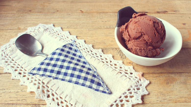 Chocolate ice cream in a dish beside an old-fashioned napkin and spoon.