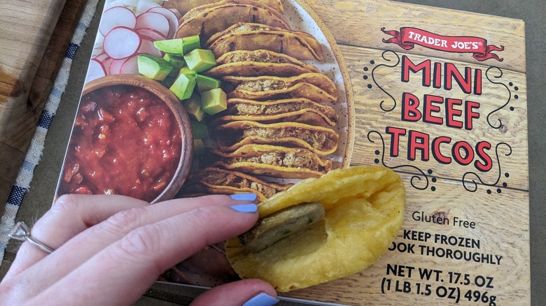 On top of the packaging, a woman holds open a Trader Joe's mini beef taco