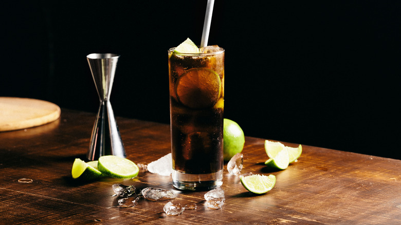 A dark soda cocktail with lime garnishes and ice around the glass