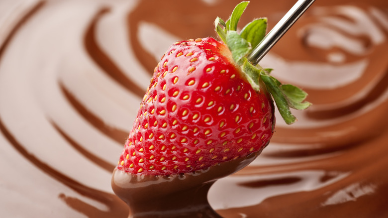 A strawberry being dipped into chocolate.