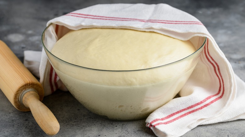Bread dough rising in glass bowl with towel
