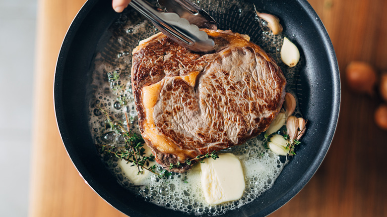 searing steak in skillet with garlic