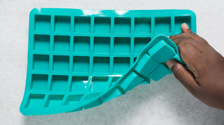 Hand bending the corner of a teal silicone ice mold