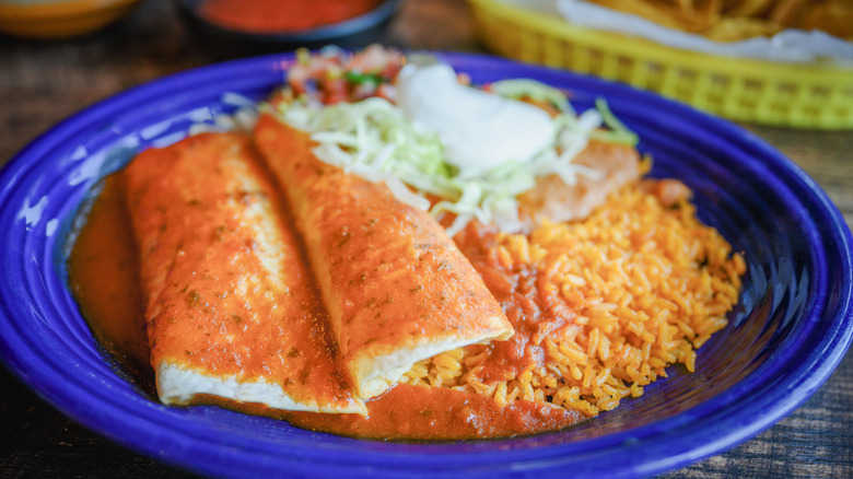 A plate of chicken enchiladas with rice, beans, lettuce, sour cream, and pico de gallo salsa