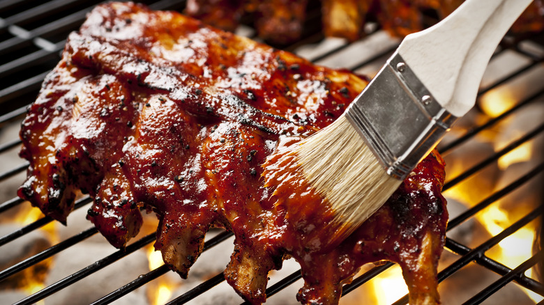 Applying barbecue sauce to ribs on the grill