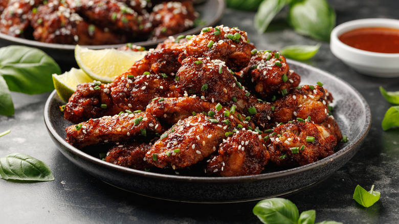 Plates of baked chicken wings topped with sesame seeds and green onion with lime wedges on the side