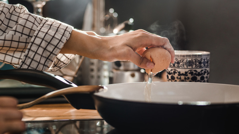 person cracking open an egg with one hand over a hot skillet