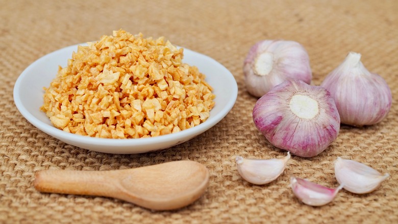 Bowl of fried garlic with wooden spoon next to multiple heads of garlic