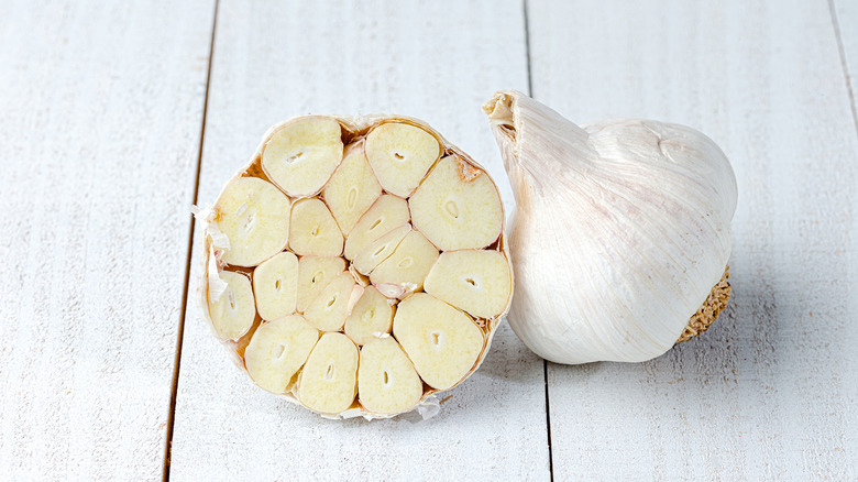 One whole garlic head and one head of garlic cut in half on wooden surface