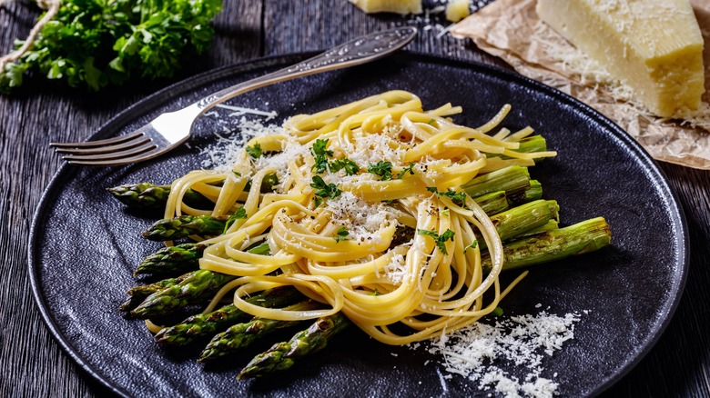 Charred asparagus with pasta noodles and grated cheese on black plate