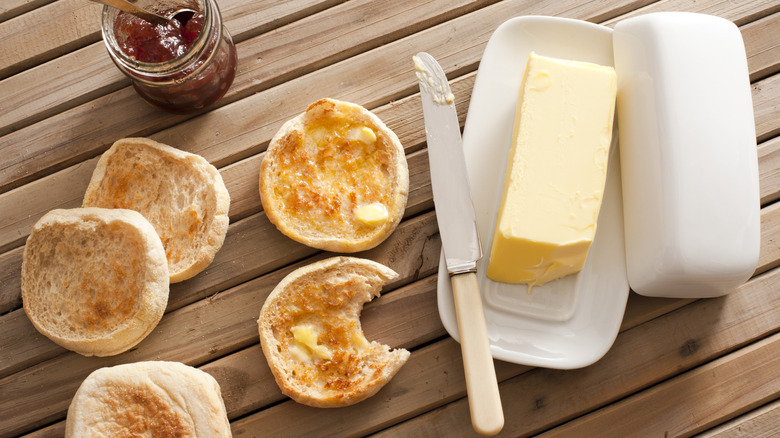 A butter dish next to english muffins and a jar of jam