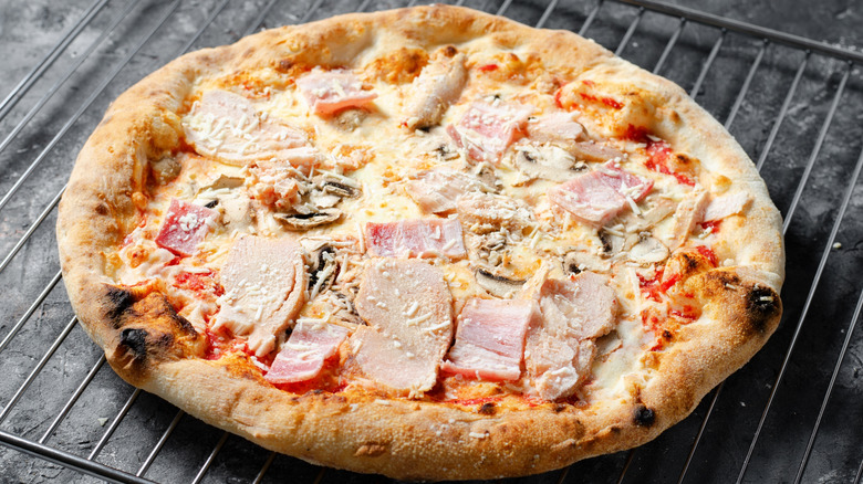 A frozen, meat-filled pizza sits on an oven grate