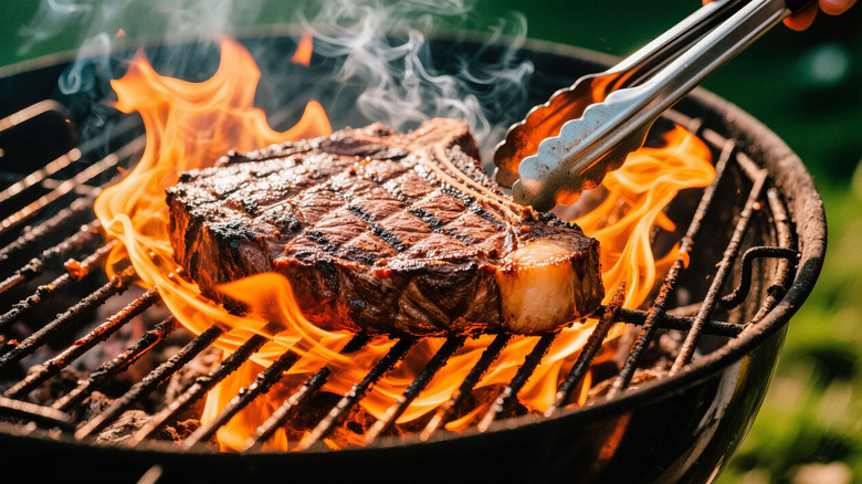 Someone cooks a T-bone steak on a charcoal grill.
