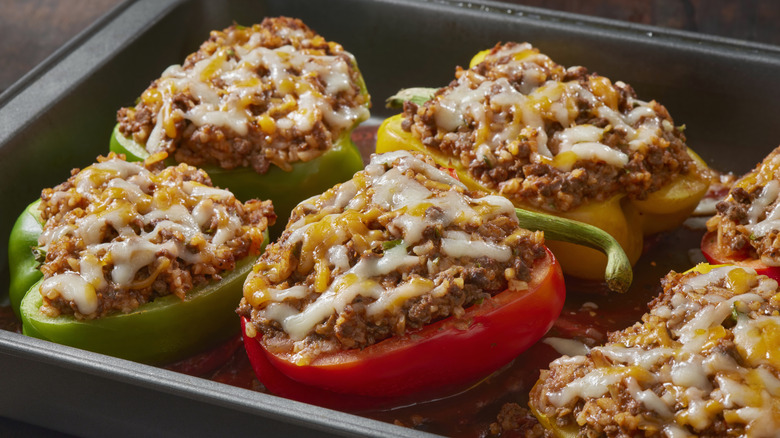 A tray of green, red, and yellow peppers are stuffed with ground meat and cheese