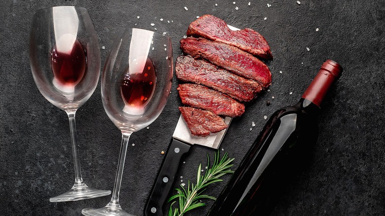 Wine glasses, a bottle of red wine, and strips of rare steak