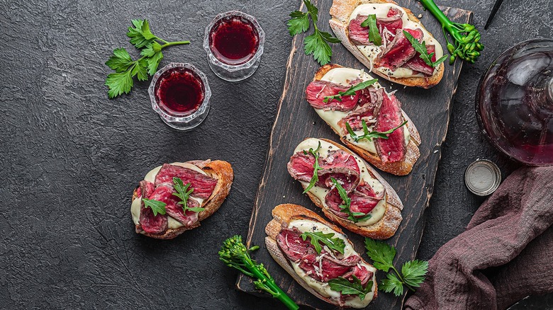 Steak crostini with cream sauce and fresh herbs alongside two glasses of red wine