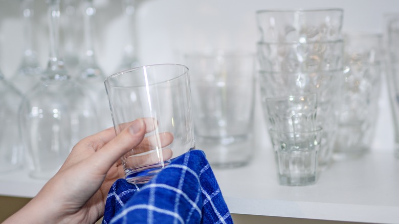 Person polishing glass in front of cupboard