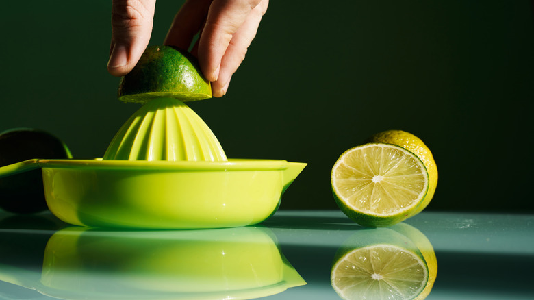A hand juices a lime using a manual plastic juicer