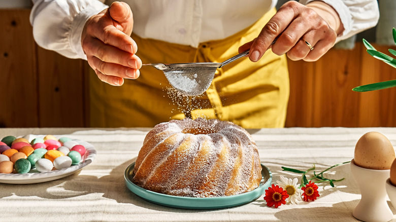 A person sifts powdered sugar onto a bundt cake
