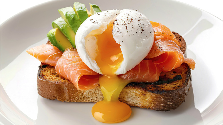 A perfectly poached egg atop golden-brown grilled toast with salmon and avocado