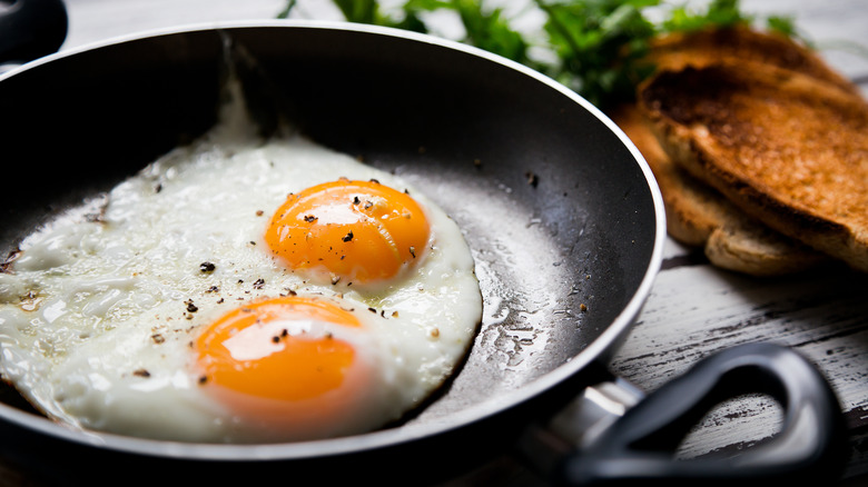 Two fried eggs in pan with toast on side