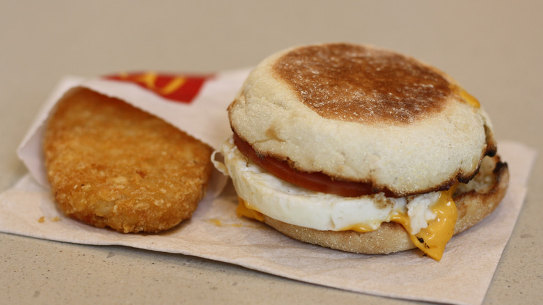 An Egg McMuffin on a napkin with a hash brown next to it.