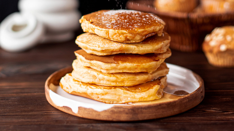 Stack of fluffy pancakes with syrup on wooden plate