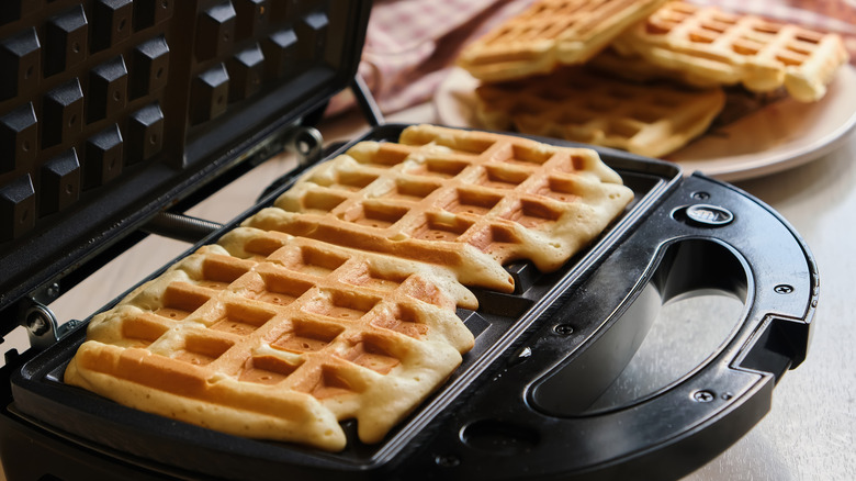 2 cooked waffles sit on an open waffle iron