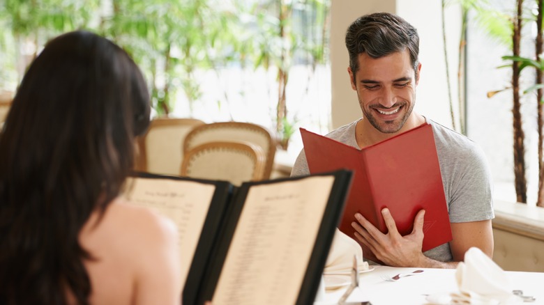 A man and woman smile while looking at a menu at a restuarant