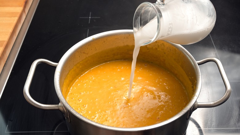 Coconut milk being added to a pot of curry
