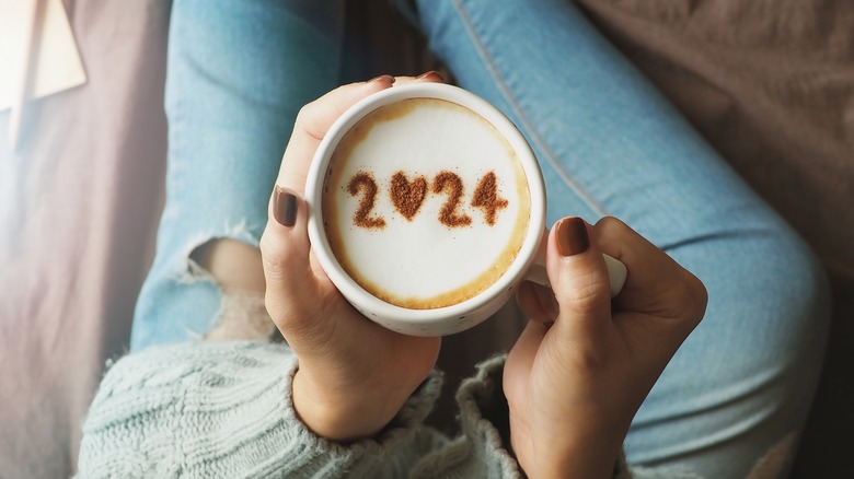 Person holding mug of coffee with 2024 latte art