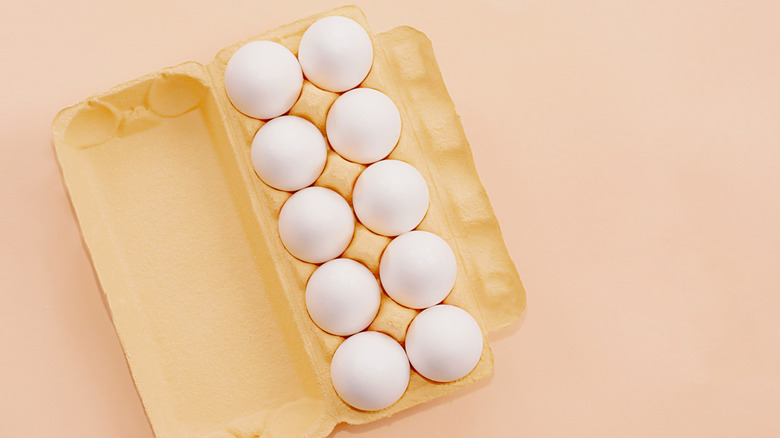 A carton of white chicken eggs sits on a pastel background