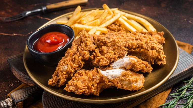 A plate of fried chicken with ketchup and fries on a plate