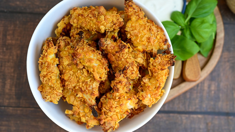Fried chicken pieces breaded with cornflakes in a white bowl