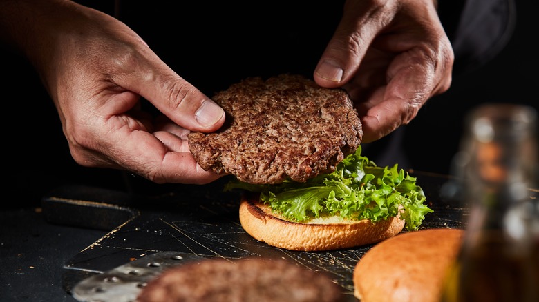Placing a homemade burger patty on a bun