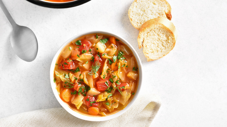 Cabbage soup sits in a white bowl, with bread nearby