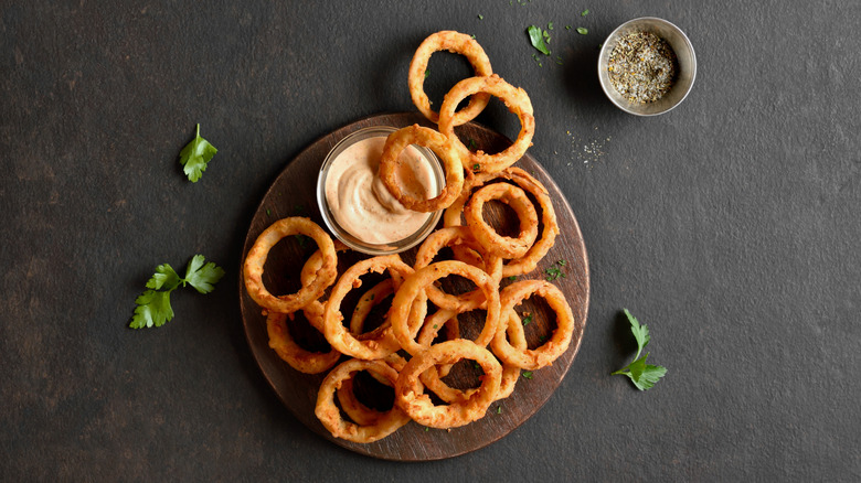 Plate of crispy onion rings with sauce on black table