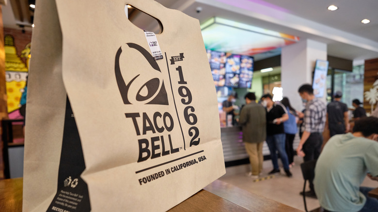 Closeup of a paper Taco Bell food bag, with a walk-up ordering station in the background