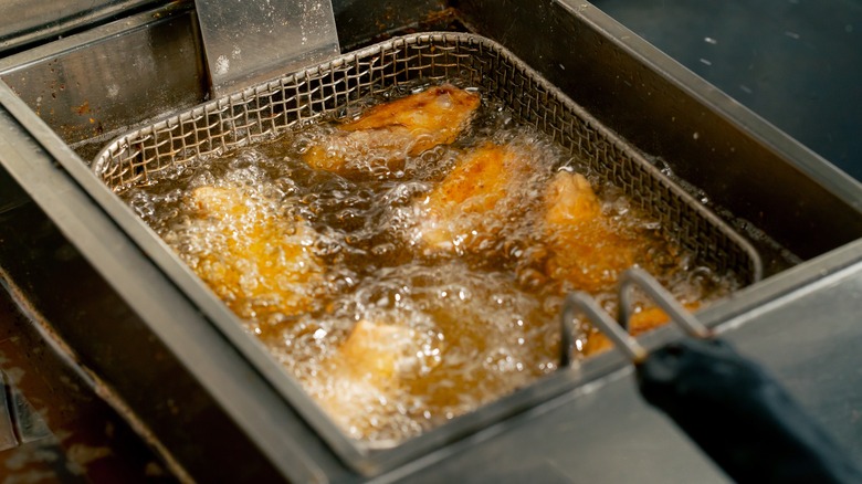 A batch of breaded chicken is fried in oil in an industrial kitchen