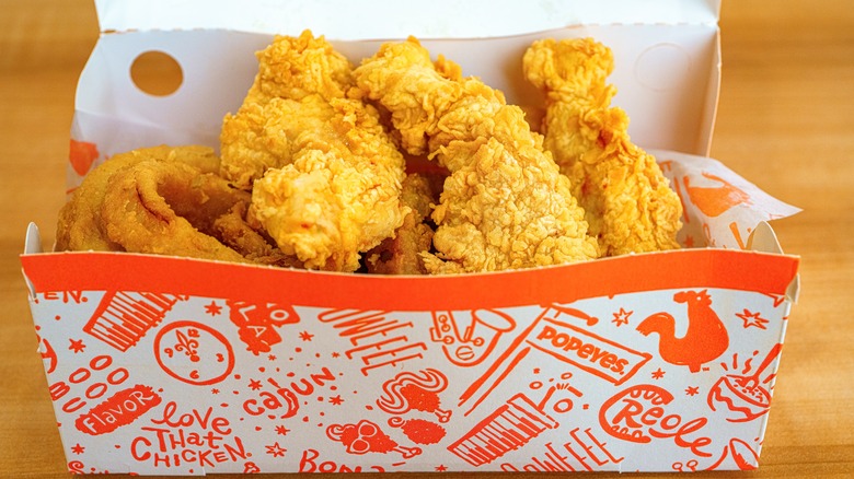 A box of Popeyes chicken tenders sits on a wooden table