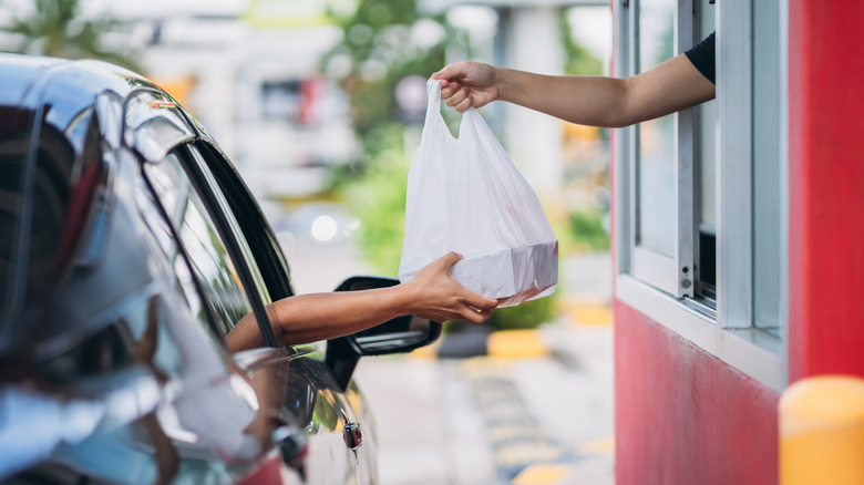 A fast food employee hands out a bag to a person in their car.
