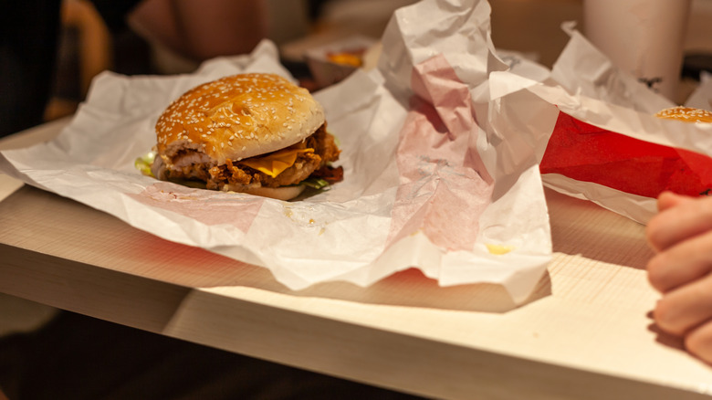 A burger with a single bite taken out of it sits on its wrapper at a fast food table