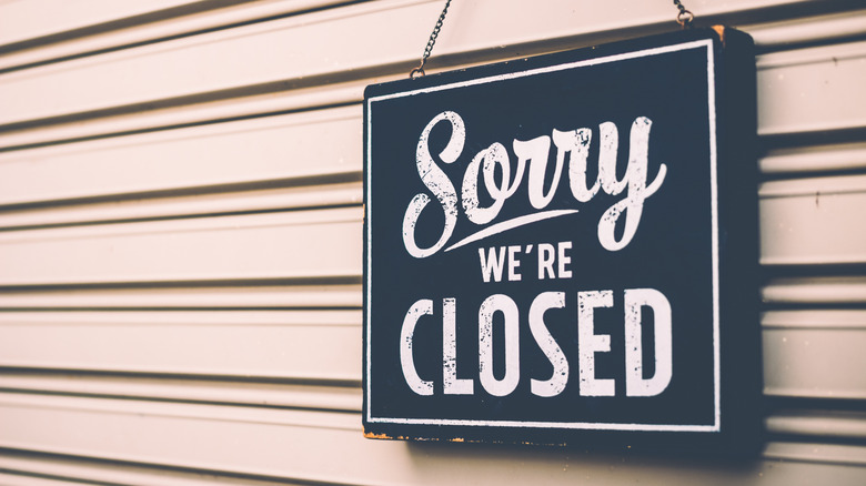 A 'Sorry we're closed' sign hangs on the roll-down door of a business