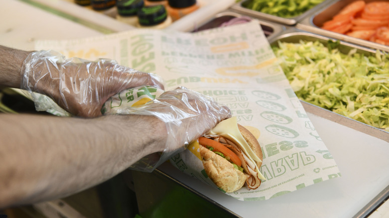 A Subway employee rolls a sub sandwich in company-printed parchment paper