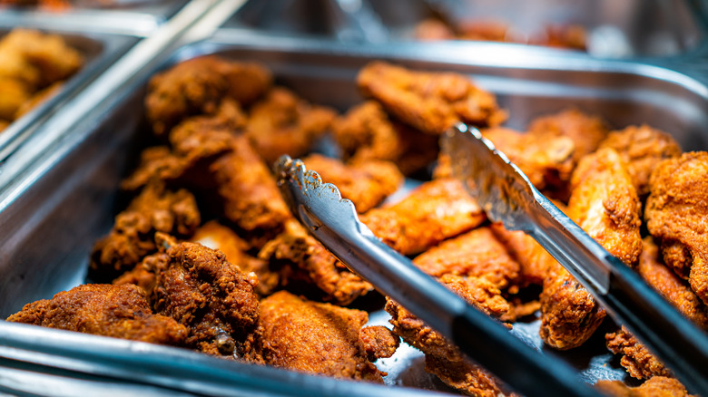 A buffet tray of fried chicken with tongs balanced on the tray