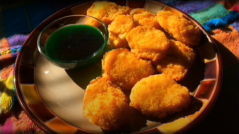 A plate is filled with chicken nuggets and a small bowl of slimy green apple dipping sauce
